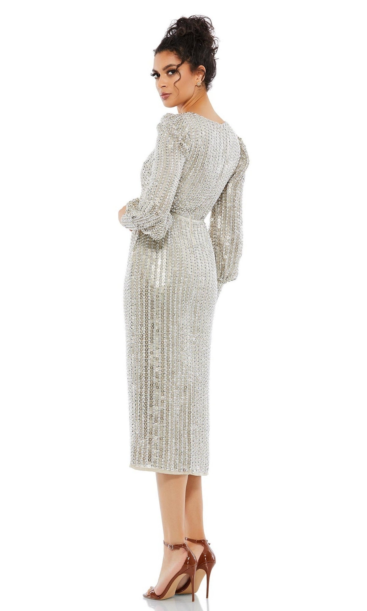 A woman poses with her back partially turned to the camera, wearing the Short Wedding Guest Dress 10809 by Mac Duggal, a silver v-neck long sleeve dress paired with beige high-heeled sandals.